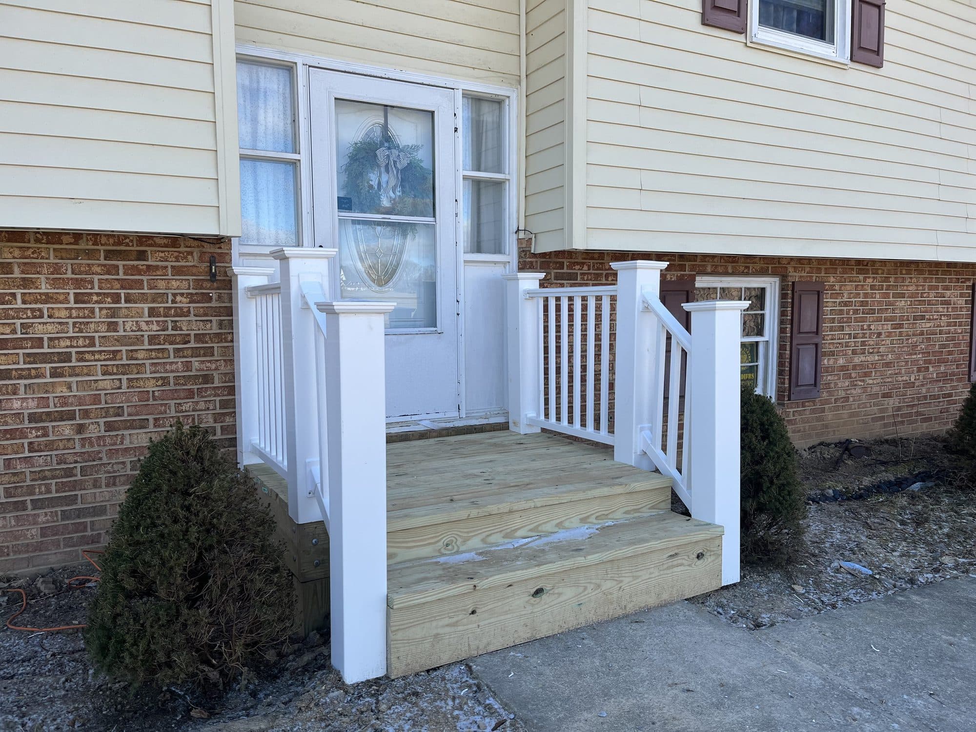 New wooden deck, stairs, and white railings at a front door